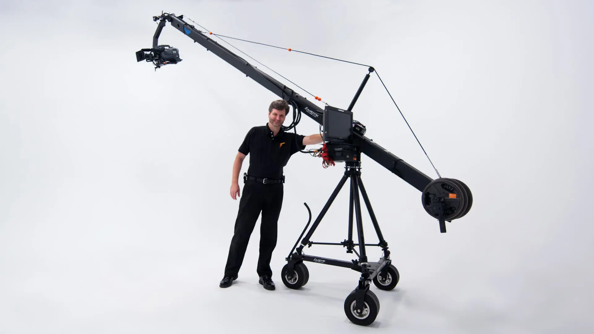 Man in a black shirt standing beside a camera jib on a white cyc
