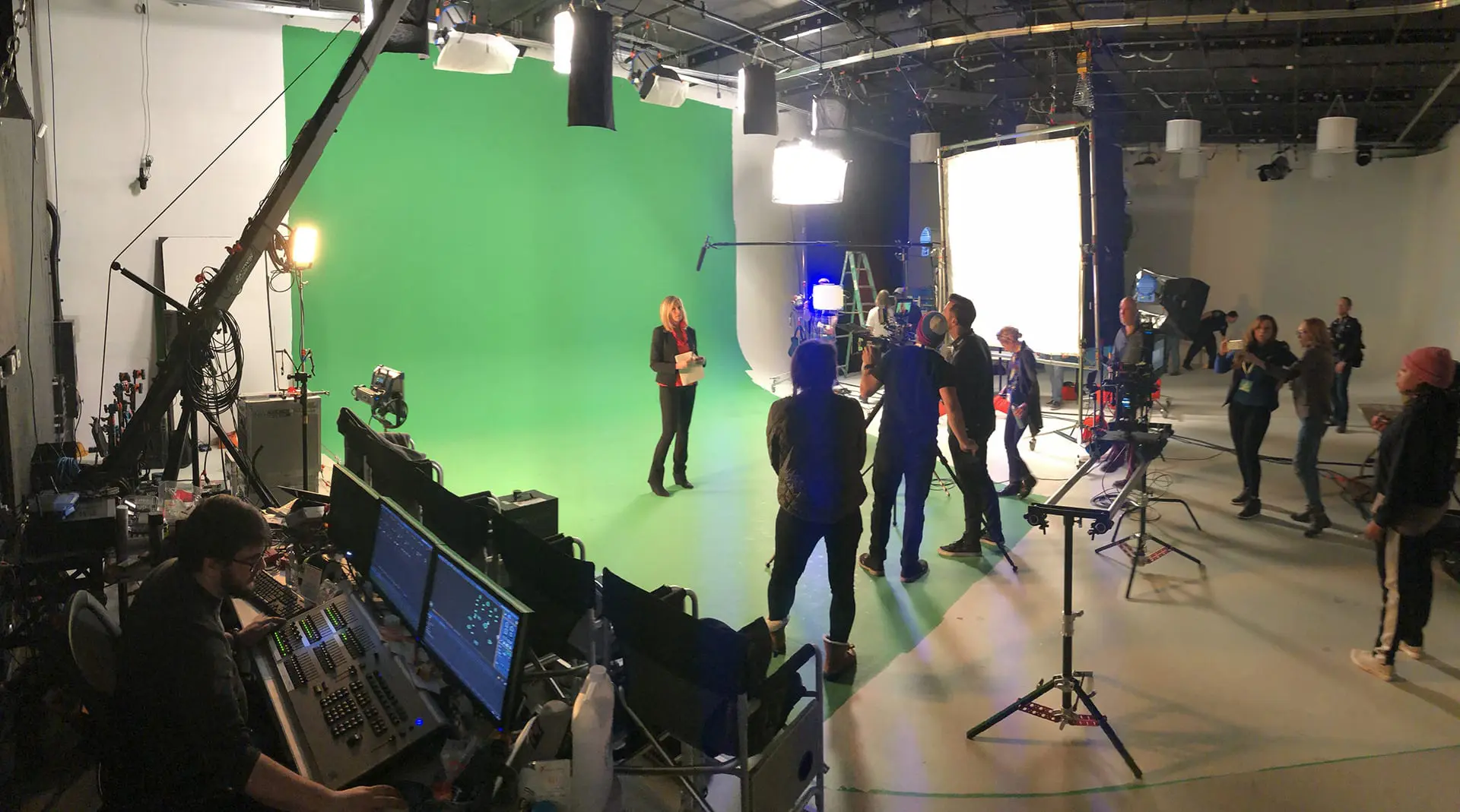 Crew and talent on a green screen stage, with an operator at a video switcher and monitors in the foreground