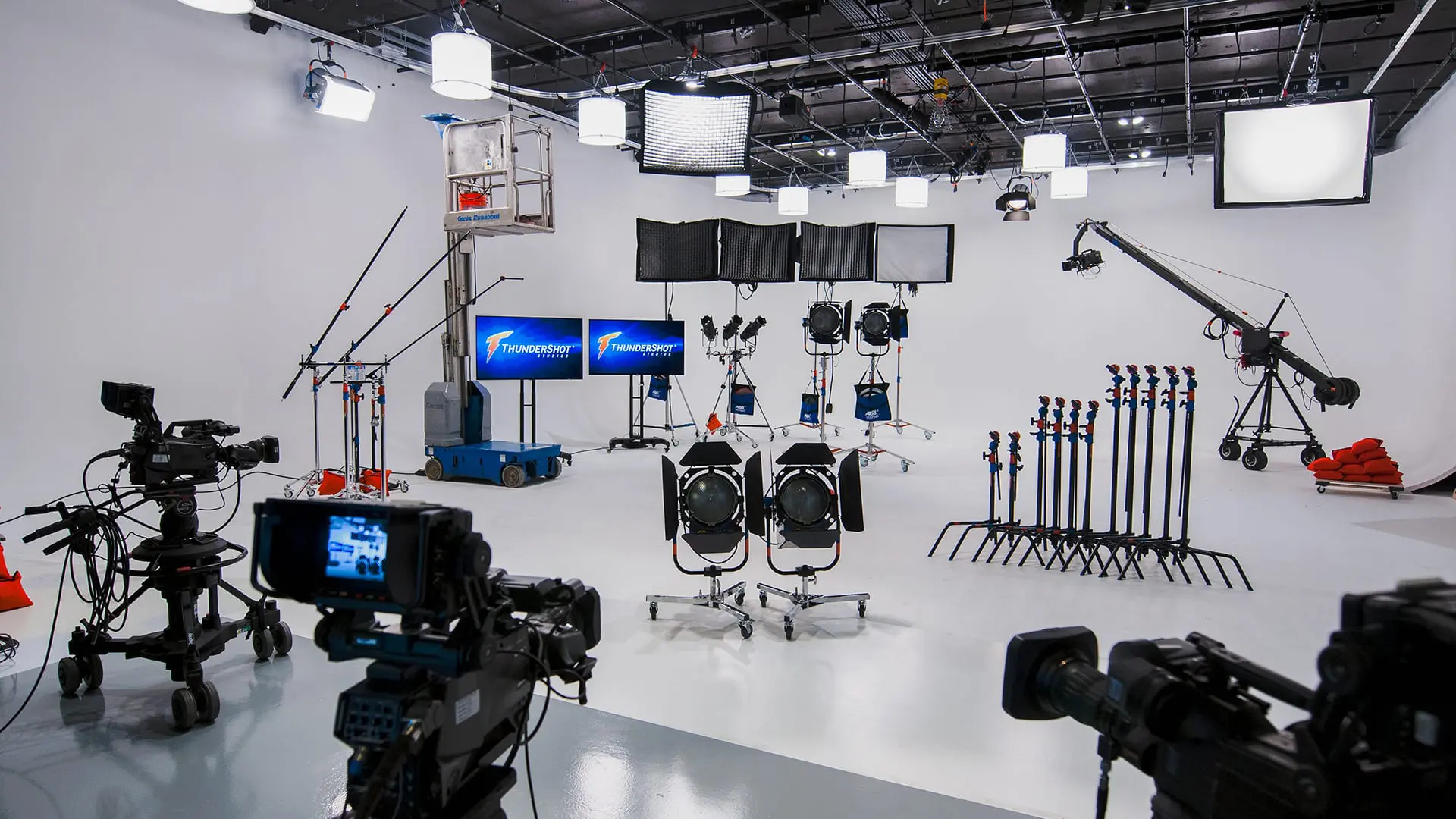White cyc studio with cameras on pedestals, lights on stands, C-stands and a camera jib