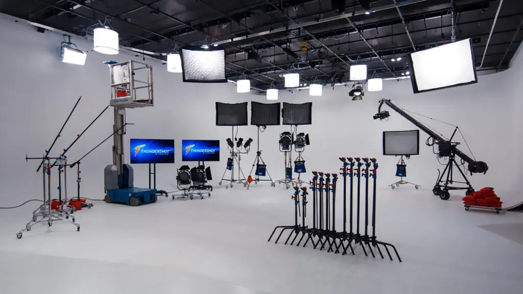 Empty white cyc studio with lights on stands, C-stands, a camera jib, monitors and a personnel lift