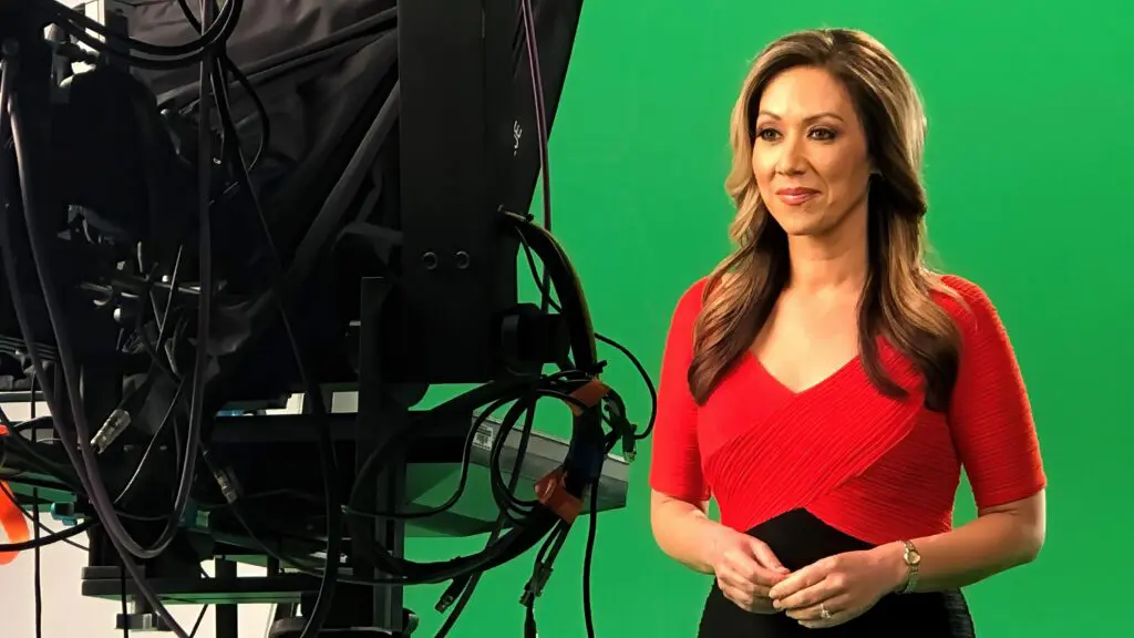 Woman in a red dress standing on a green screen next to camera equipment