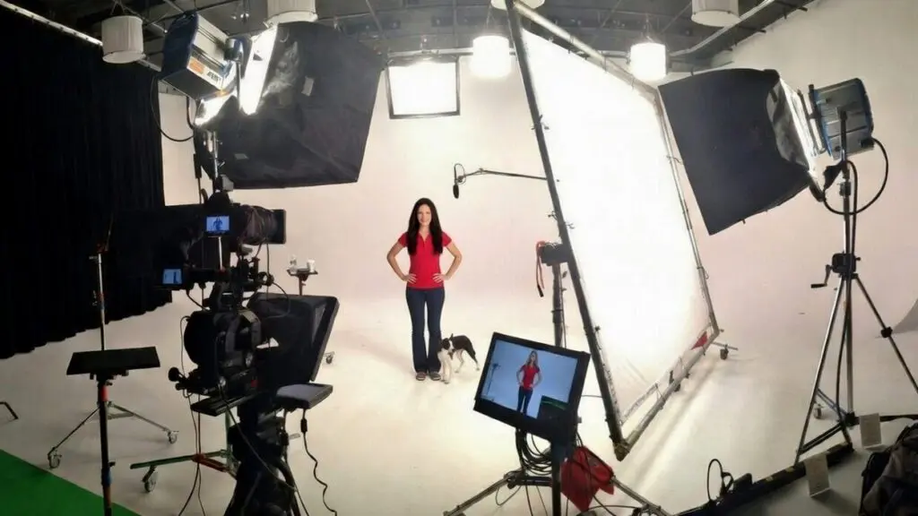 Woman in a red shirt with a small dog on a white cyc, surrounded by lights, scrims, a camera and monitor